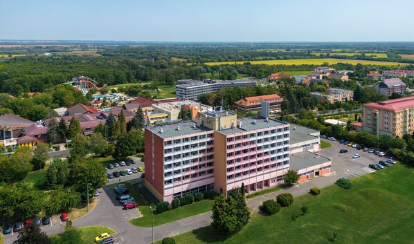 A multi-story building with a parking lot and a view of surrounding greenery and fields. - Hunguest Hotel Freya (Zalakaros)