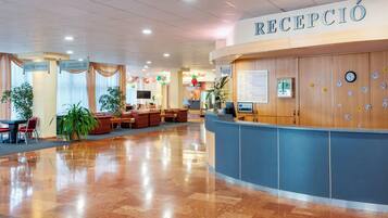 Een hotel receptie met een blauw aanrecht, een klok en een bord met de tekst 'RECEPCIÓN'.