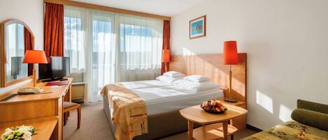 A hotel room with a bed, a desk with a telephone, a chair, a small table with fruit, and a couch.