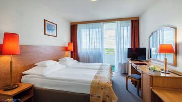Habitación de hotel con una cama grande, dos lámparas de noche, un escritorio con televisor y vistas al exterior a través de un ventanal.