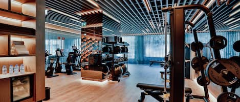 A modern gym with wooden floors, exercise equipment, and a wall-mounted rack of dumbbells.