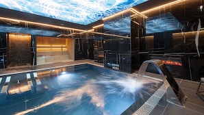 Un área de piscina interior moderna con una gran proyección en el techo, un jacuzzi y una chimenea.