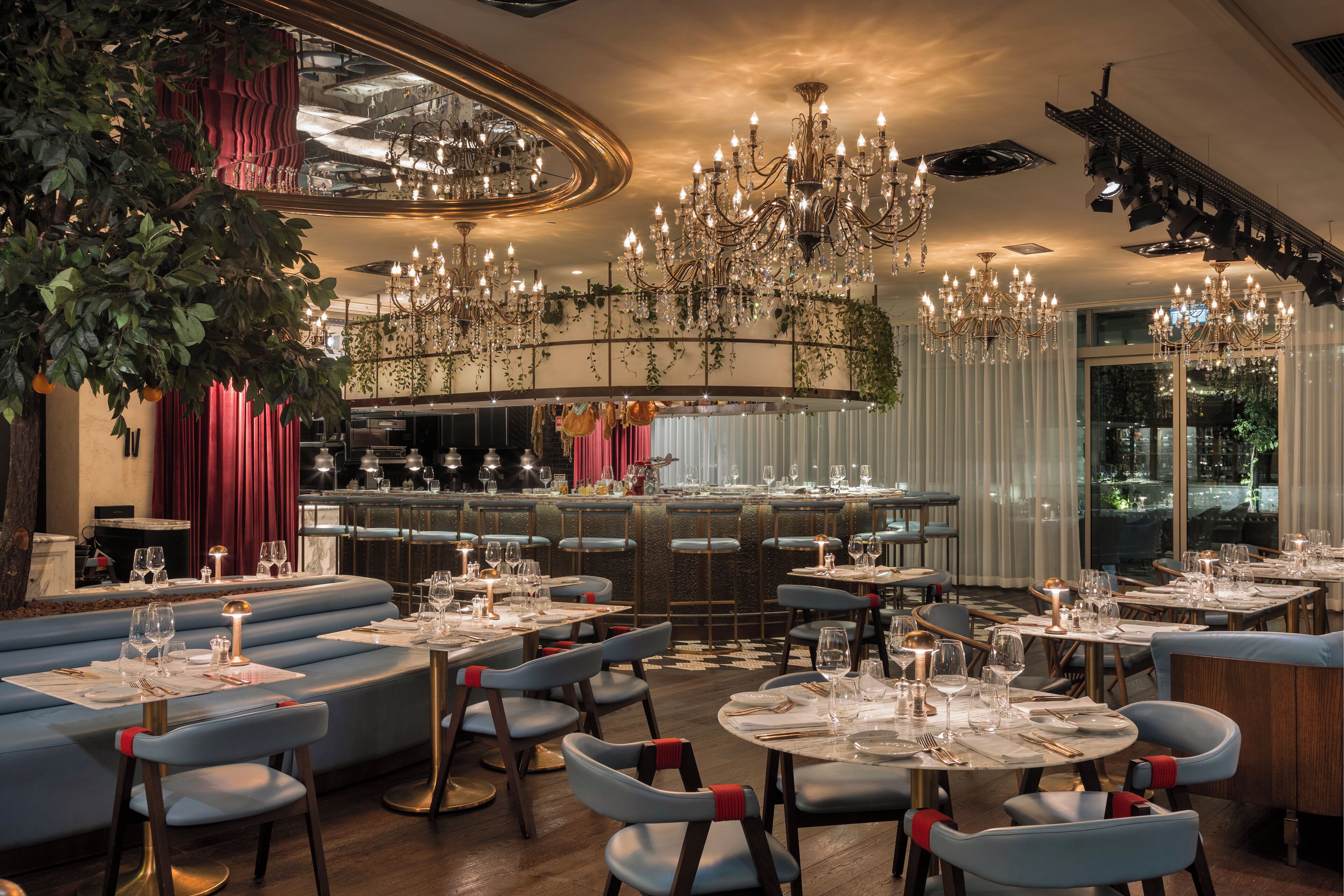 A restaurant with round tables, blue chairs, and a bar area.