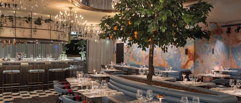 Restaurante com assentos em tom azul, lustres e uma árvore com laranjas.