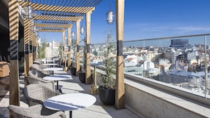 Terraza en la azotea con mobiliario de mimbre, plantas en macetas y vistas a la ciudad.