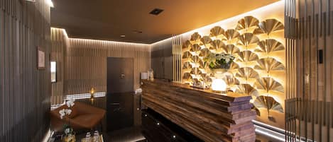 Una moderna área de recepción con un mostrador de madera, una exhibición de ventiladores en la pared y un espacio de descanso con una silla marrón y una pequeña mesa.