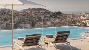 Un área de piscina en la azotea con dos sillones, una mesa con una bebida y una sombrilla grande.