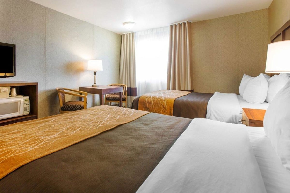 A hotel room with two beds, a desk with a lamp, a television, and a microwave.