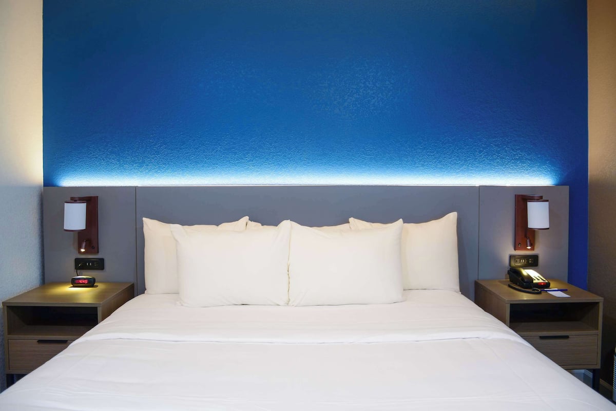 A hotel room with a large bed, two bedside tables, a nightstand, and a wall-mounted telephone.