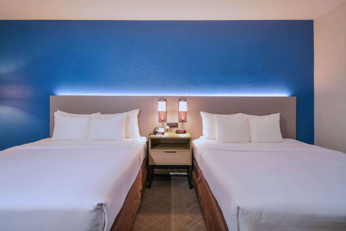 A hotel room with two beds, a nightstand, and a wall-mounted lamp.