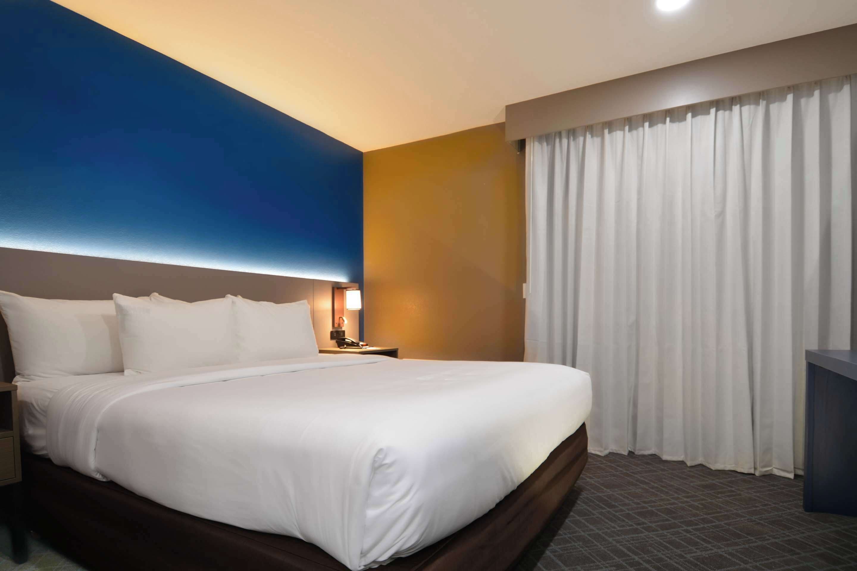A hotel room with a large bed, a nightstand, a lamp, and a window with curtains.