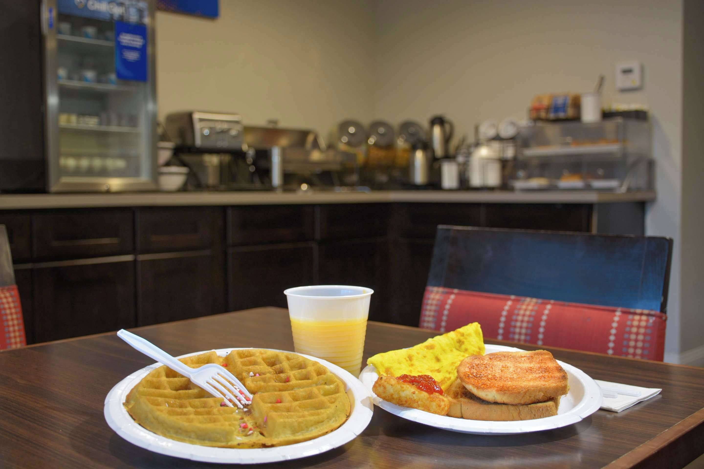 A breakfast setting with a waffle, toast, and a cup of orange juice on a table.