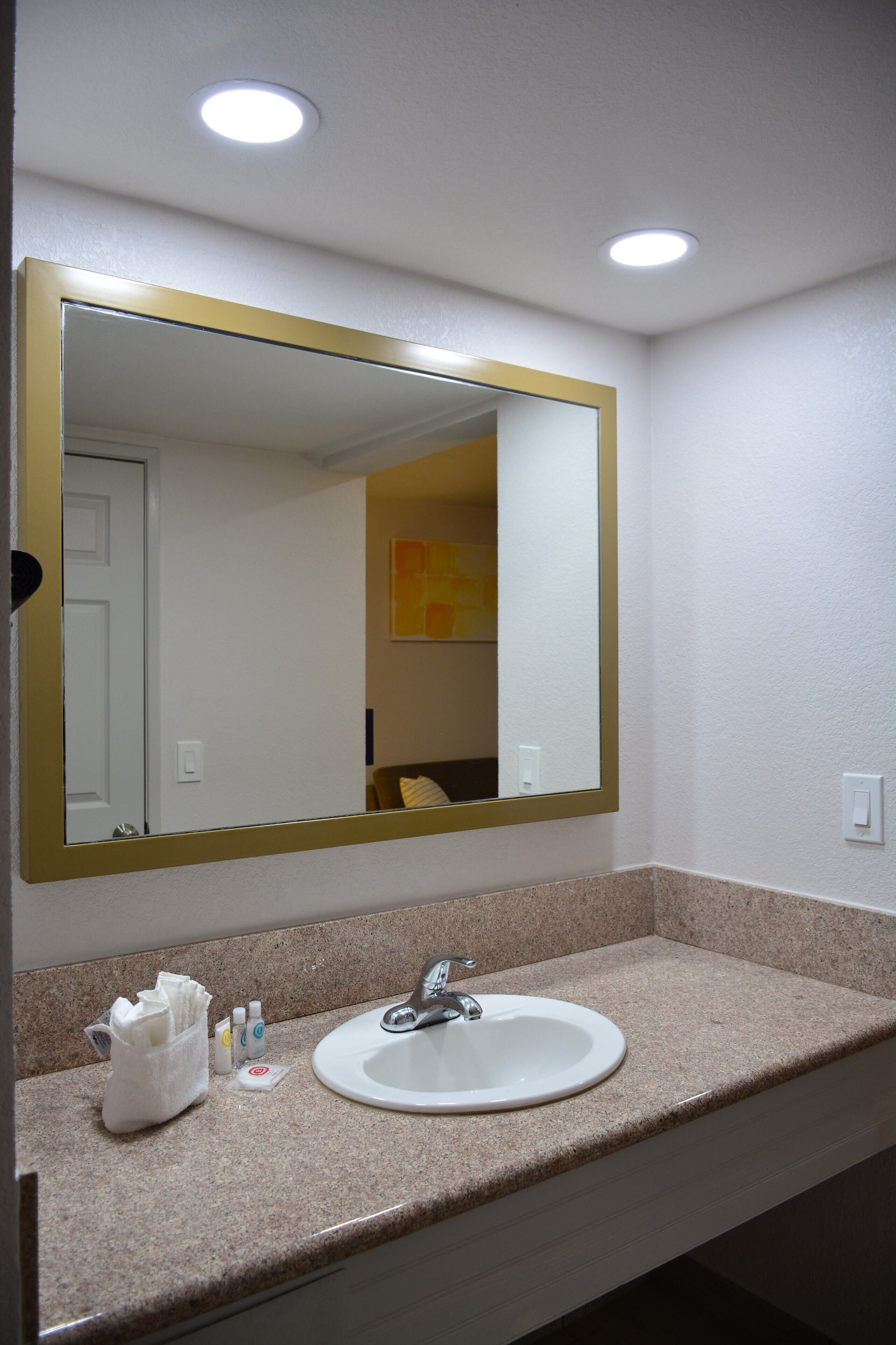 A bathroom with a white sink, a large mirror with a gold frame, and a countertop with toiletries.