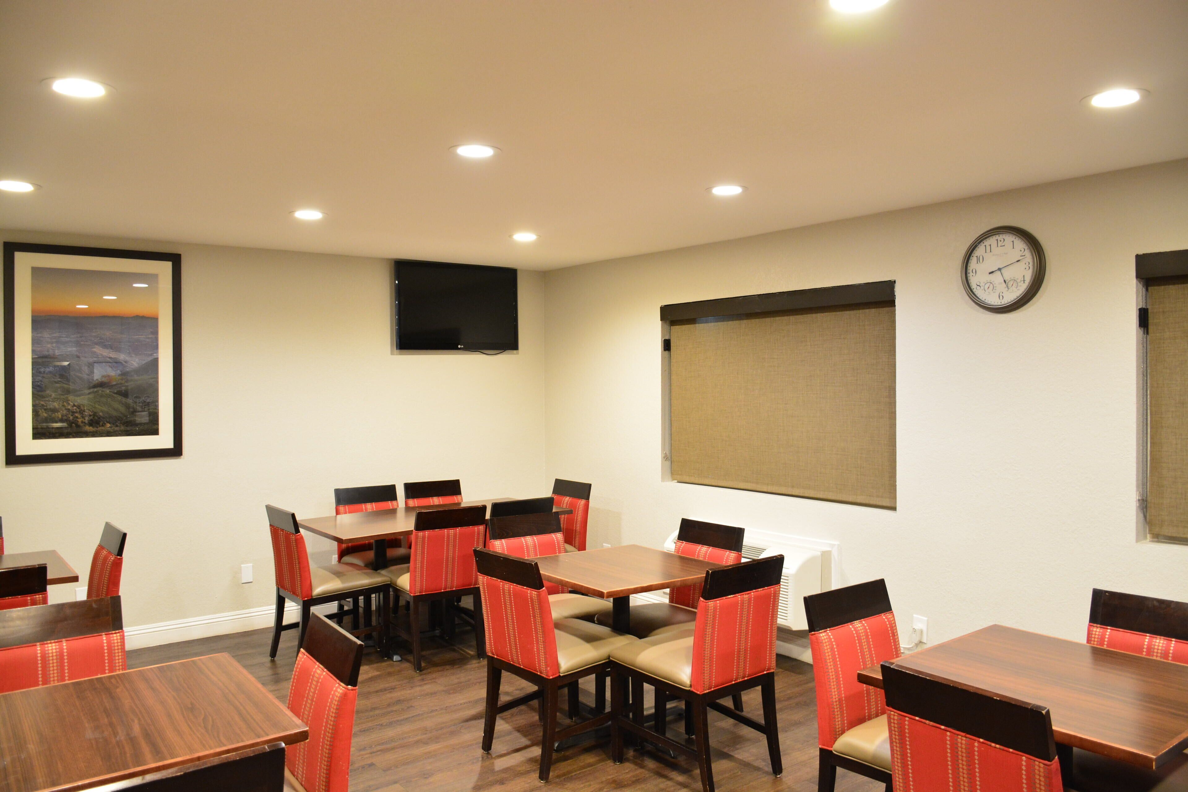 A conference room with wooden tables and red upholstered chairs, a clock on the wall, and a framed picture of a landscape.