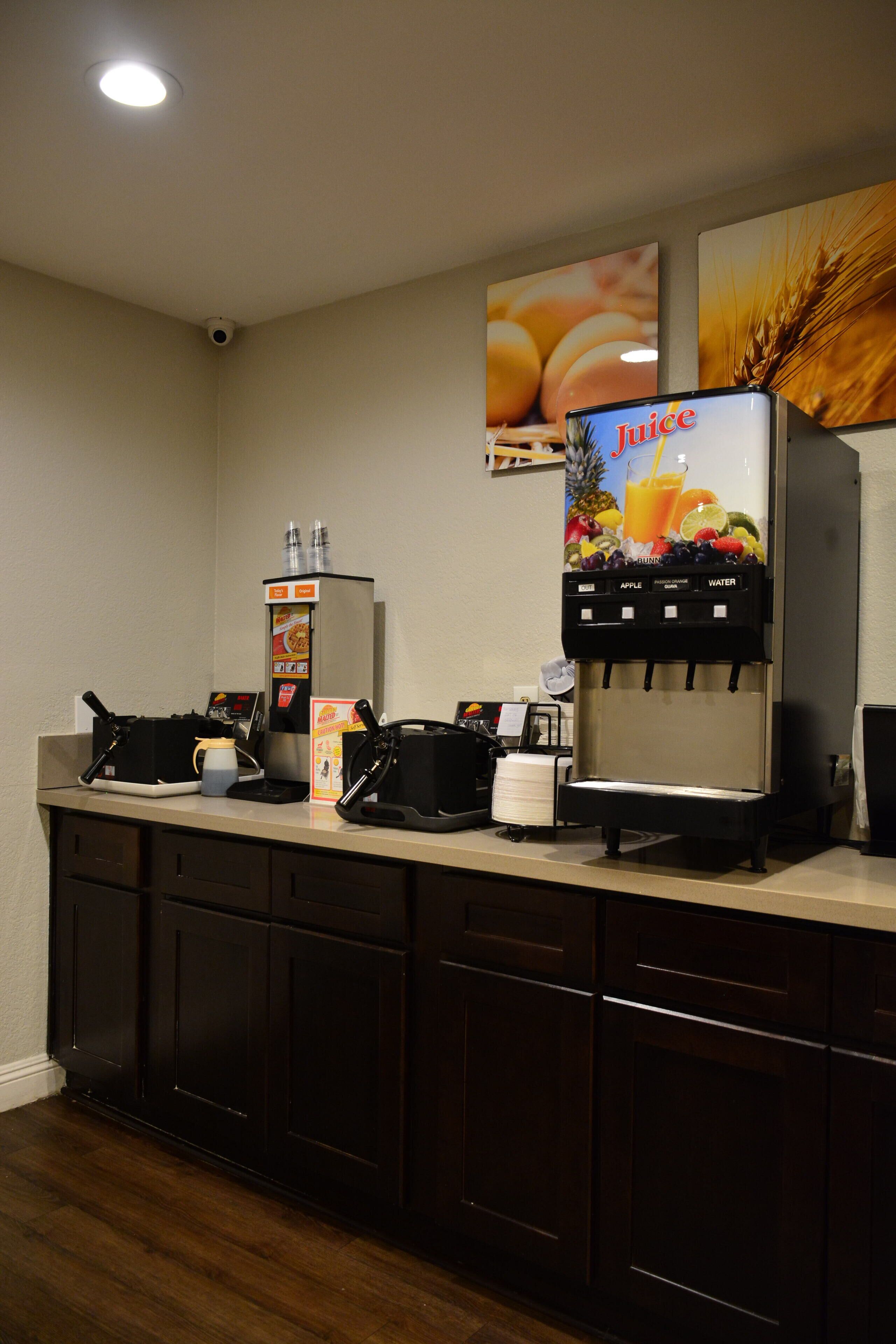 A self-service beverage station with a juice dispenser, a coffee machine, and a water cooler.