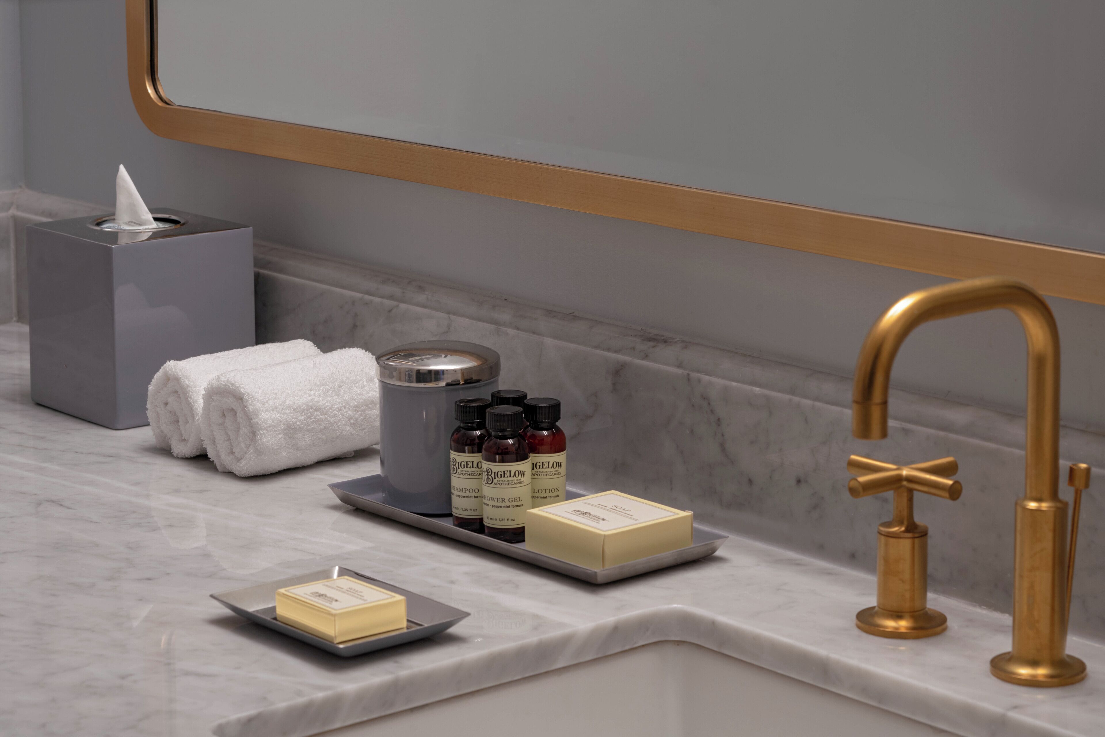 A bathroom vanity with a mirror, a towel, a soap dish, a shampoo bottle, a lotion bottle, and a gold faucet.