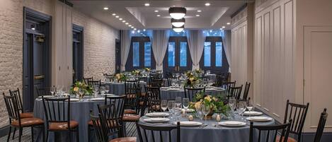 Ein Hotel-Speisesaal mit mehreren runden Tischen, dunklen Holzsesseln und einem gemusterten Boden.