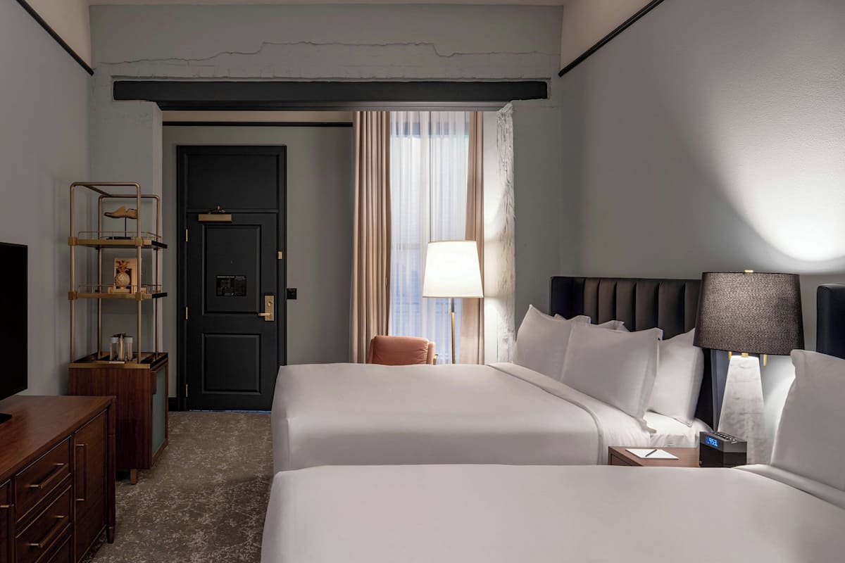 Habitación de hotel con dos camas, un escritorio, una silla, una lámpara y una puerta.
