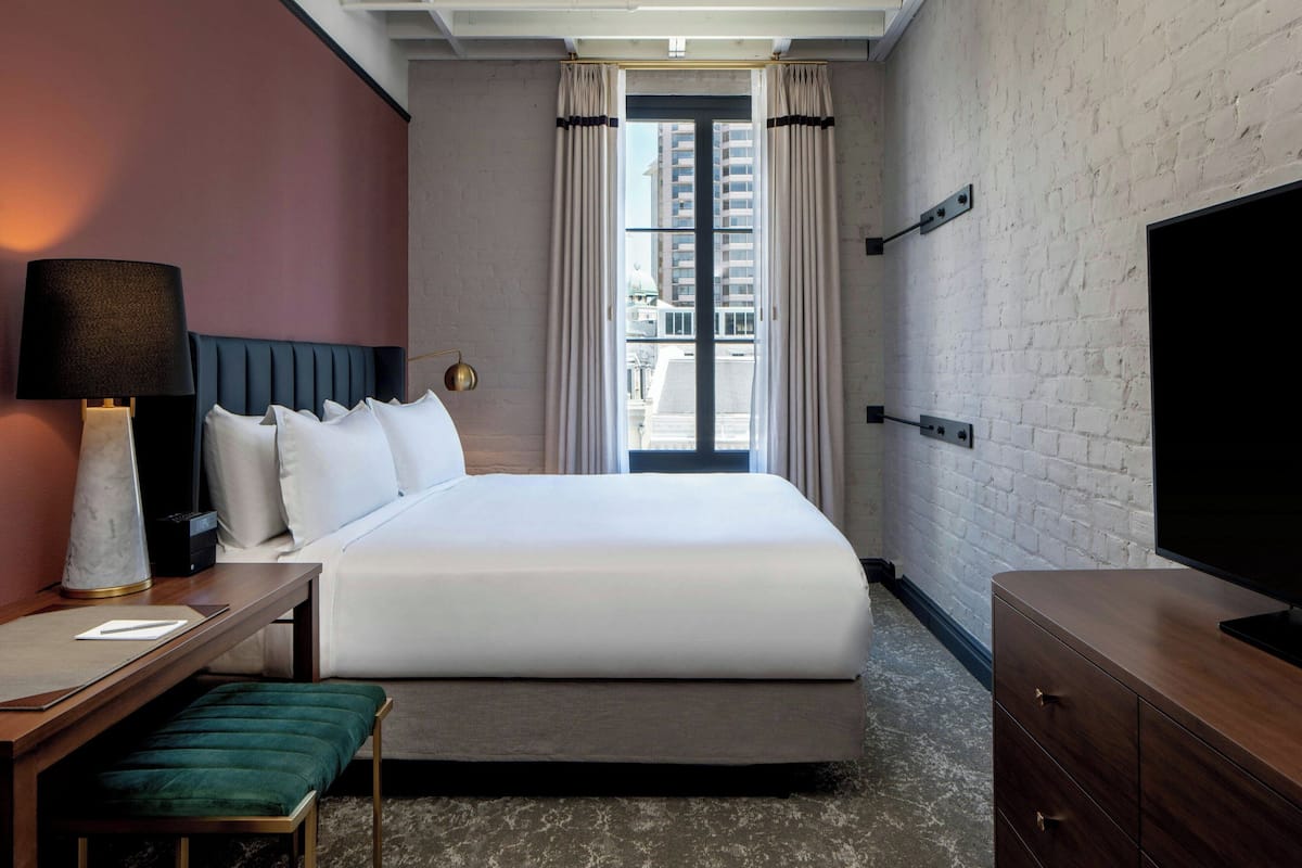 Una habitación de hotel con cama, mesita de noche, lámpara y televisor.