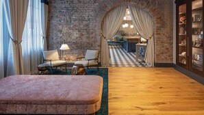 A room with a brick wall, a checkered floor, a large window with curtains, a sofa, and a lamp. - The Eliza Jane, Autograph Collection (New Orleans)