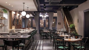 A restaurant with a checkered floor, multiple tables and chairs, hanging pendant lights, and a staircase. - The Eliza Jane, Autograph Collection (New Orleans)