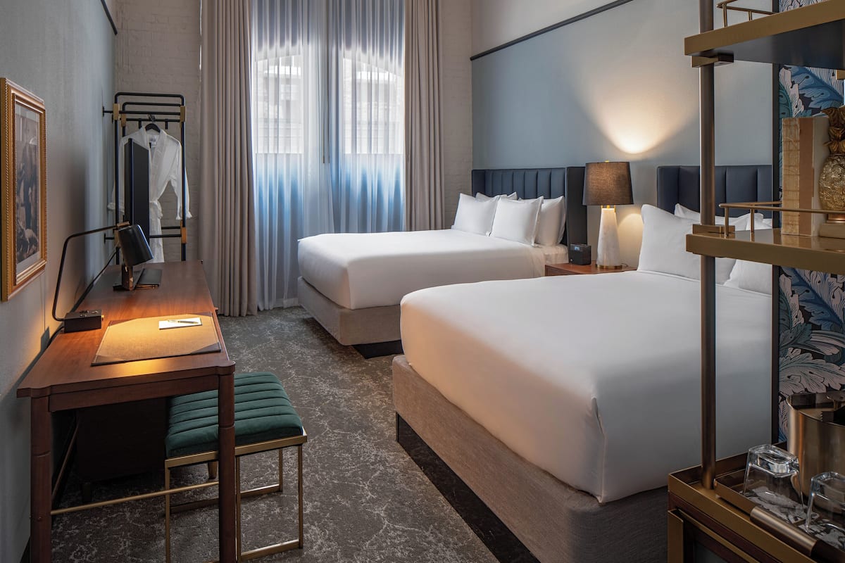 Habitación de hotel con dos camas, un escritorio, una silla, una lámpara y un espejo.