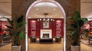 A spacious lobby with a fireplace, bookshelves, and potted plants. - The Eliza Jane, Autograph Collection (New Orleans)