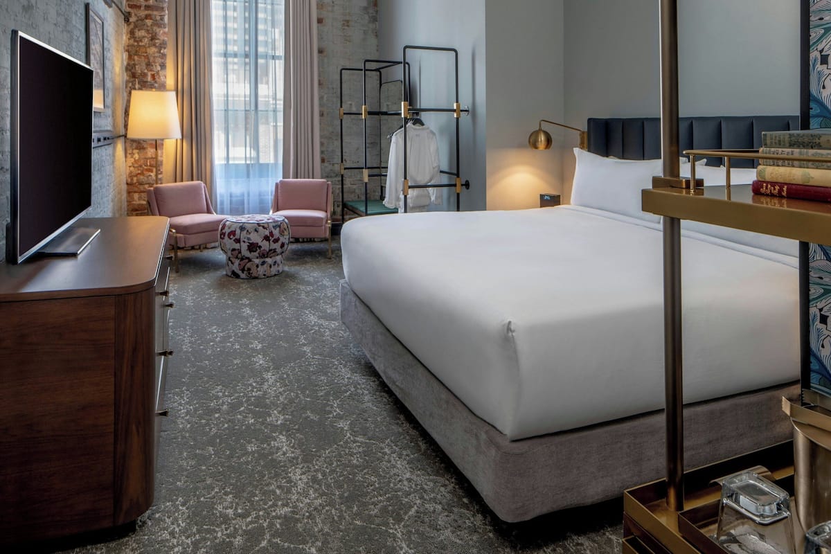 Habitación de hotel con cama, televisión, escritorio, silla, lámpara y estantería.