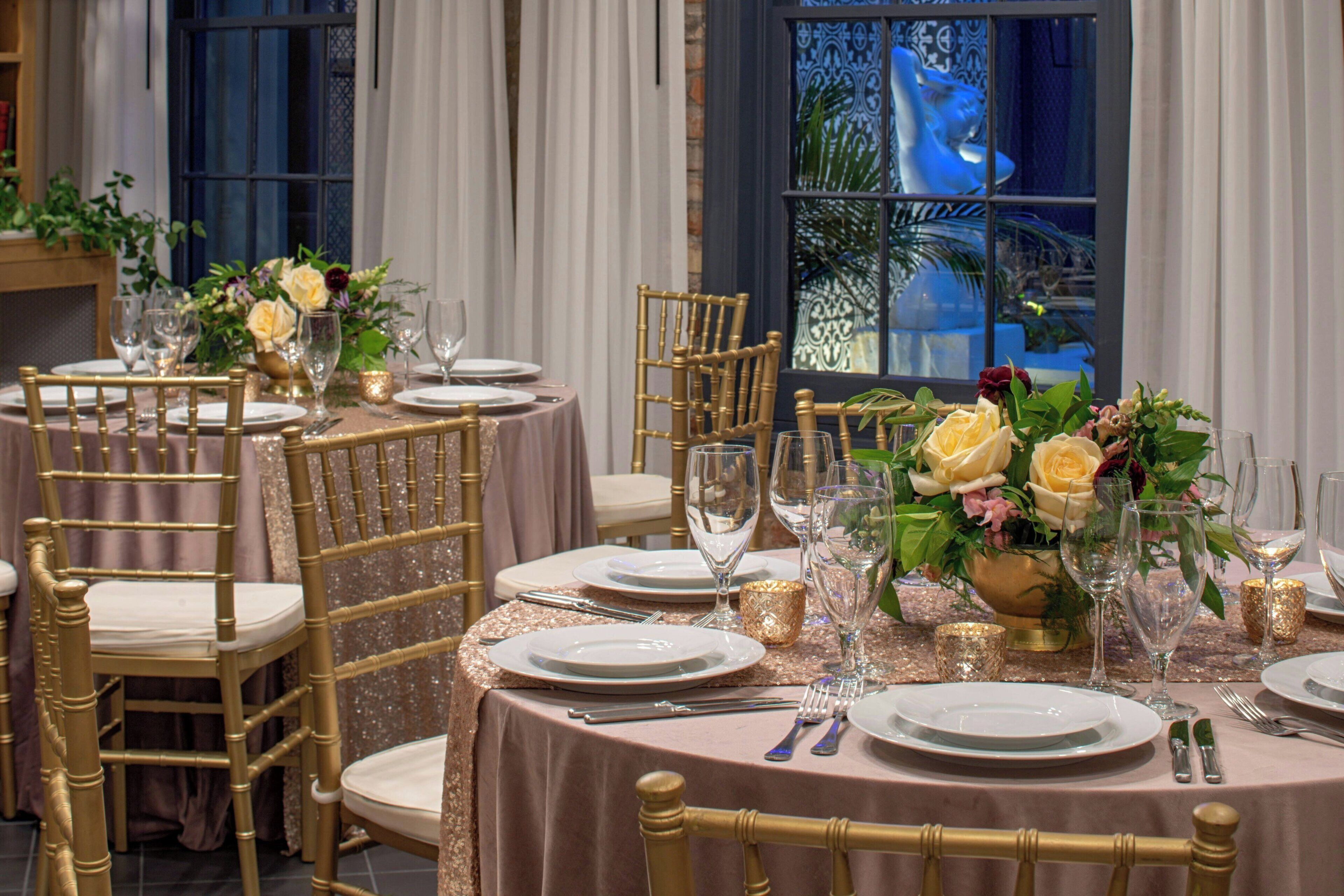 Un comedor con mesas redondas, sillas doradas y centros de mesa florales.