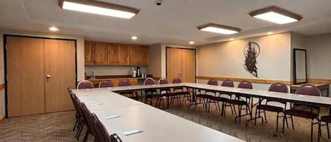 Une salle de conférence équipée d’une longue table, de chaises, d’un coin cuisine et d’un élément décoratif mural.