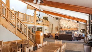 Una escalera de madera lleva a una zona superior con una chimenea de piedra, muebles de madera y un comedor.