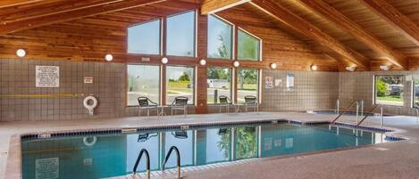 Piscina interna con travi in legno, ampie finestre e parete rivestita di piastrelle.
