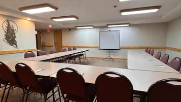 Ein Konferenzraum mit langen Tischen, Stühlen, einer Projektionsleinwand und einem Teppichboden.