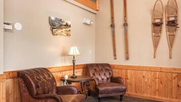 A room with two leather armchairs, a small table with a lamp, wooden skis on the wall, and a painting.