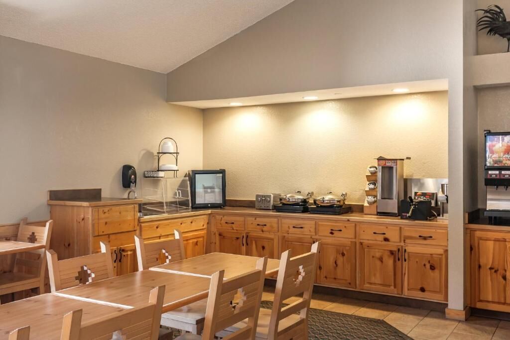 A modern kitchen with wooden cabinets, a dining table, chairs, a refrigerator, a coffee maker, and a television.