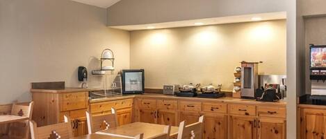 A modern kitchen with wooden cabinets, a dining table, chairs, a refrigerator, a coffee maker, and a television.