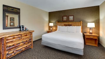 Een hotelkamer met een groot bed, houten nachtkastjes, een houten dressoir en een spiegel aan de muur.