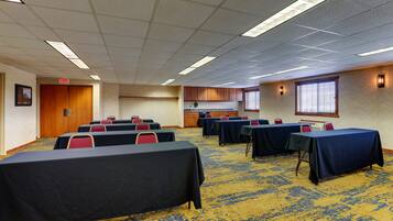 Un salón de conferencias con mesas y sillas, una kitchenette y piso alfombrado.