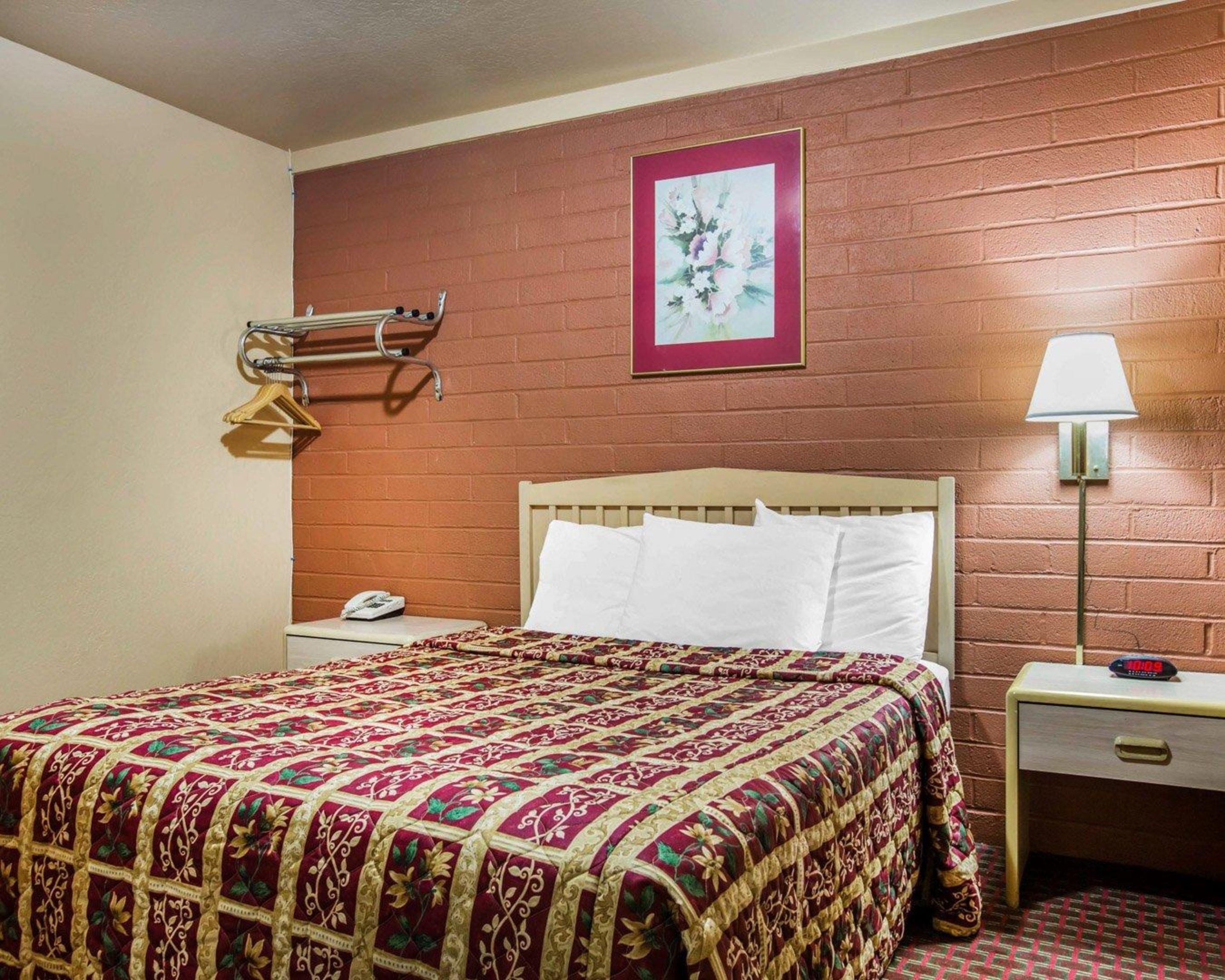 Quarto de hotel com cama, mesa de cabeceira, luminária, telefone e um quadro na parede.