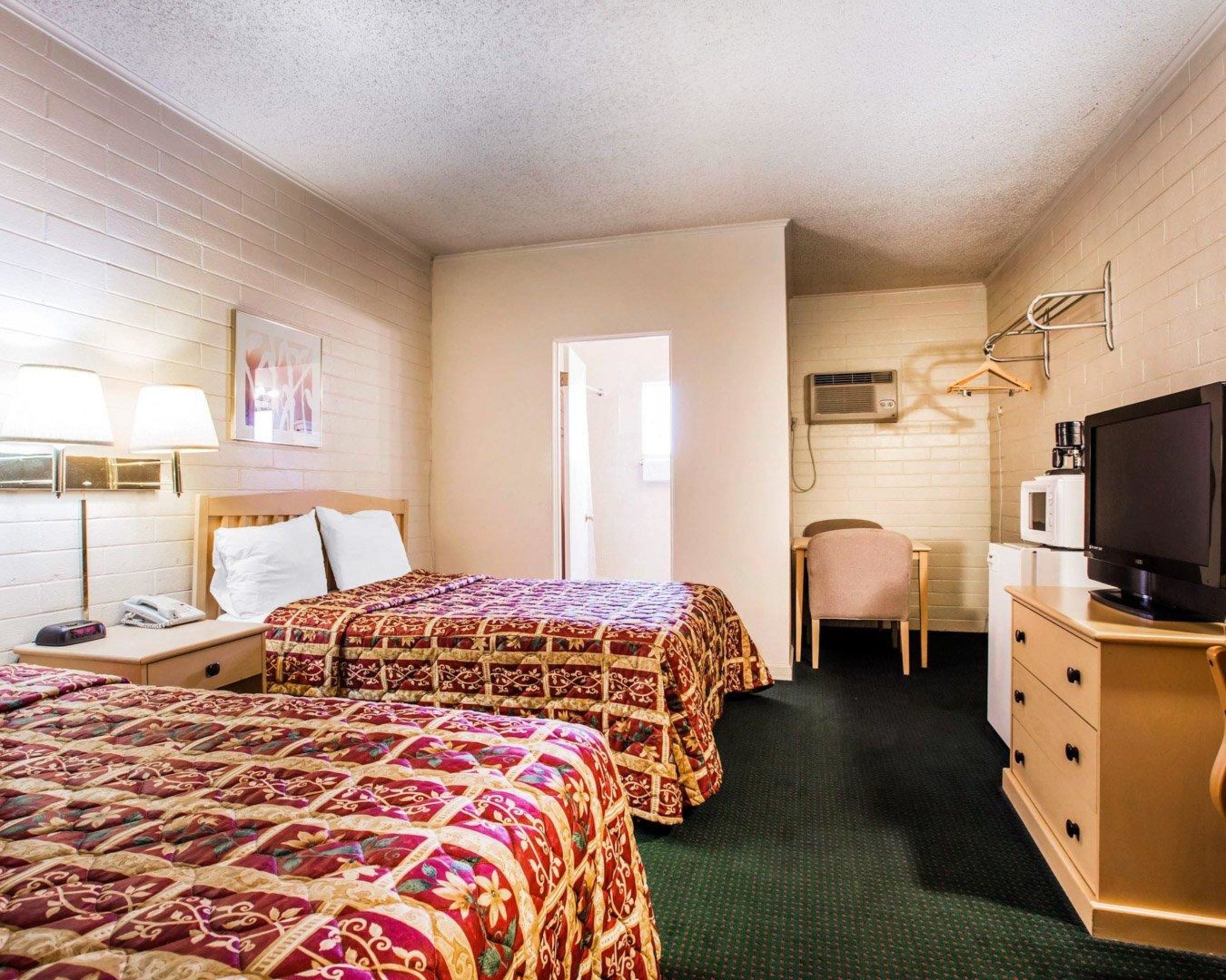 A hotel room with two beds, a desk with a chair, a television, and a dresser.