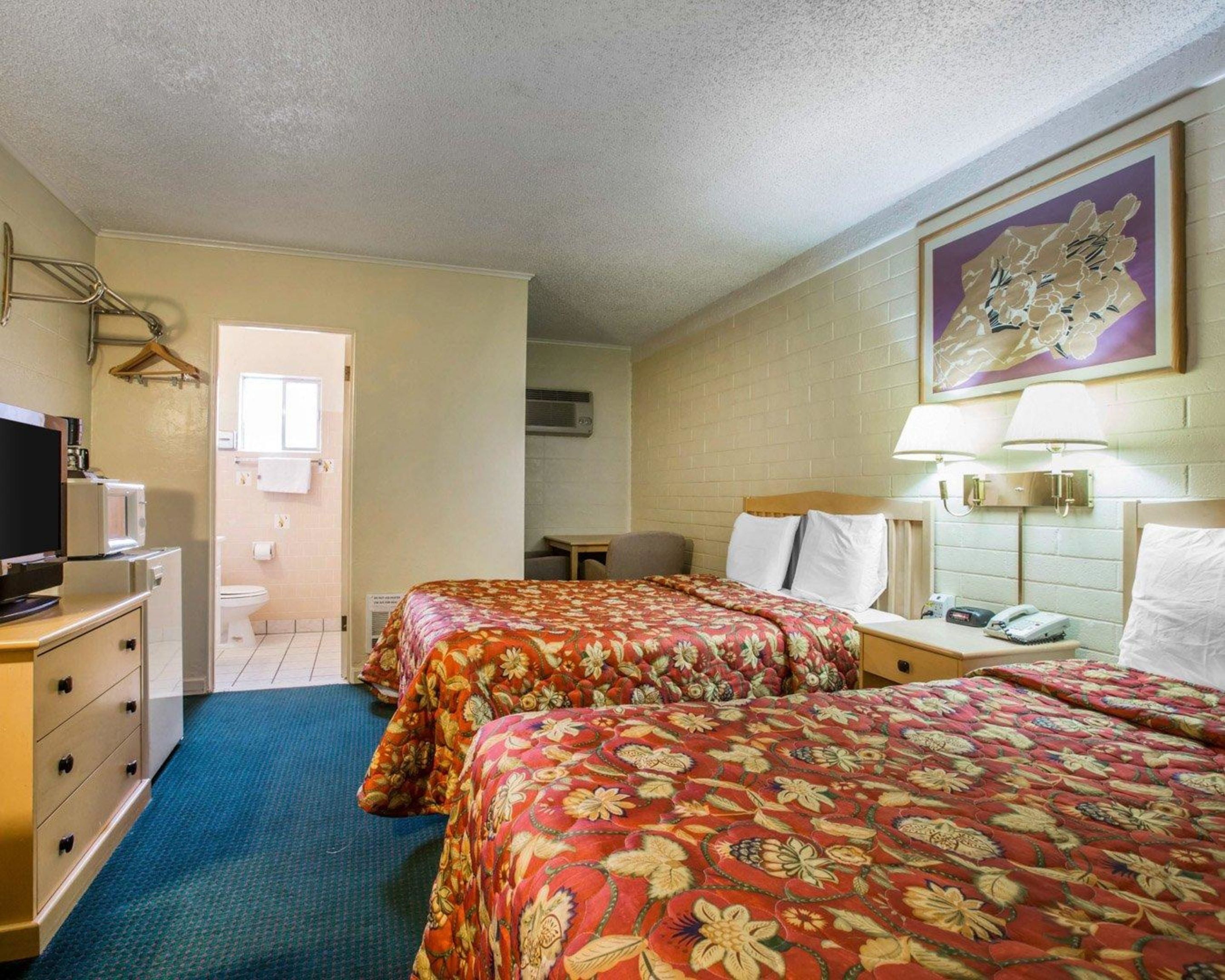 A hotel room with two beds, a TV, a desk, and a bathroom.