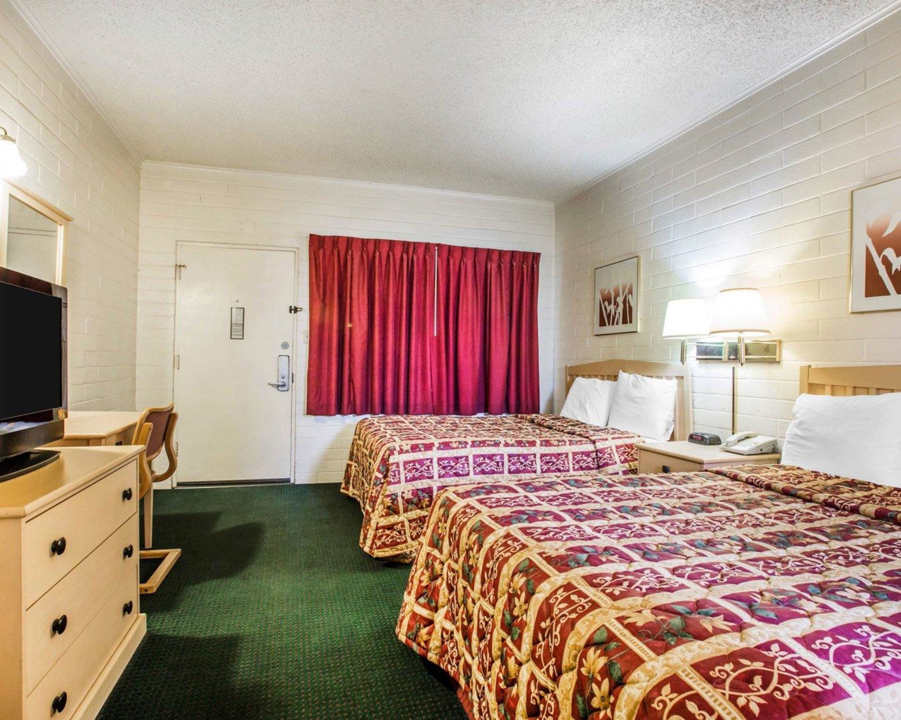 A hotel room with two beds, a TV, a dresser, and a door.