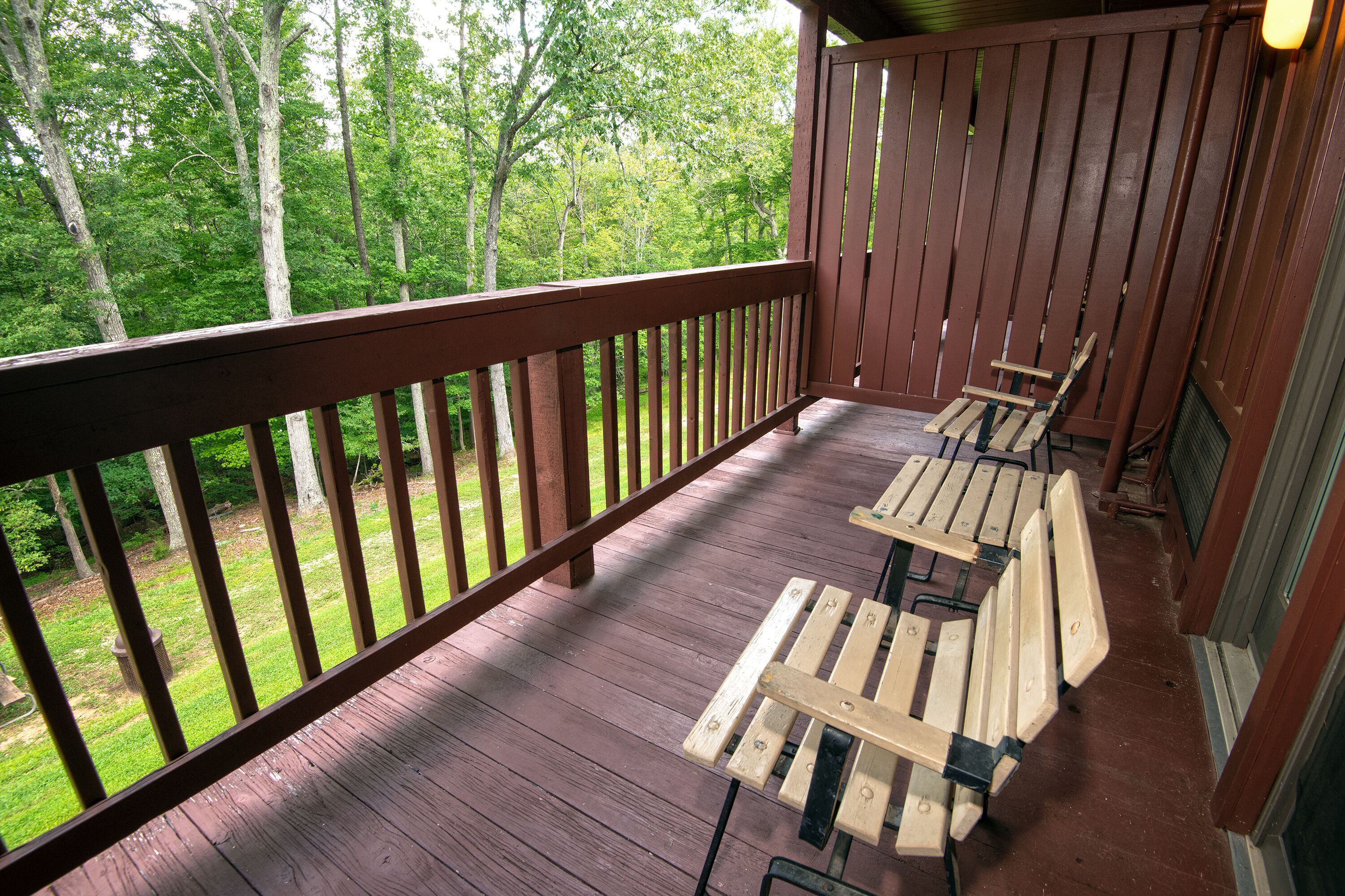 A wooden deck with a railing, a bench, and a view of a forest.