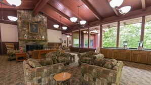 A spacious living room with patterned sofas, a stone fireplace, and large windows offering a view of greenery. - Carter Caves State Resort Park (Olive Hill)