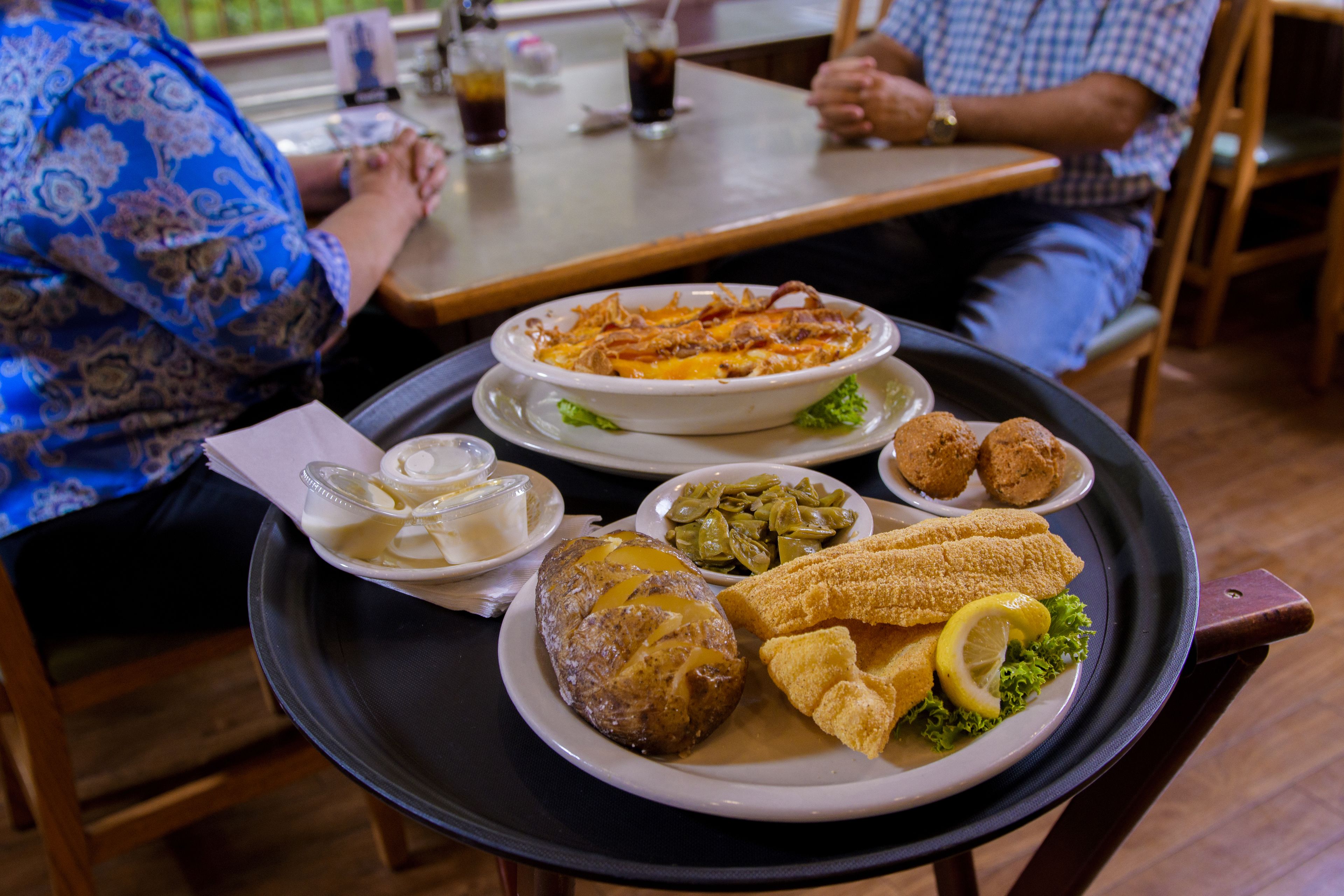 A dining table with a variety of dishes including a baked potato, green beans, fried fish, and breaded items.