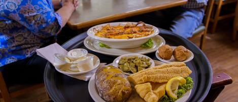 A dining table with a variety of dishes including a baked potato, green beans, fried fish, and breaded items.