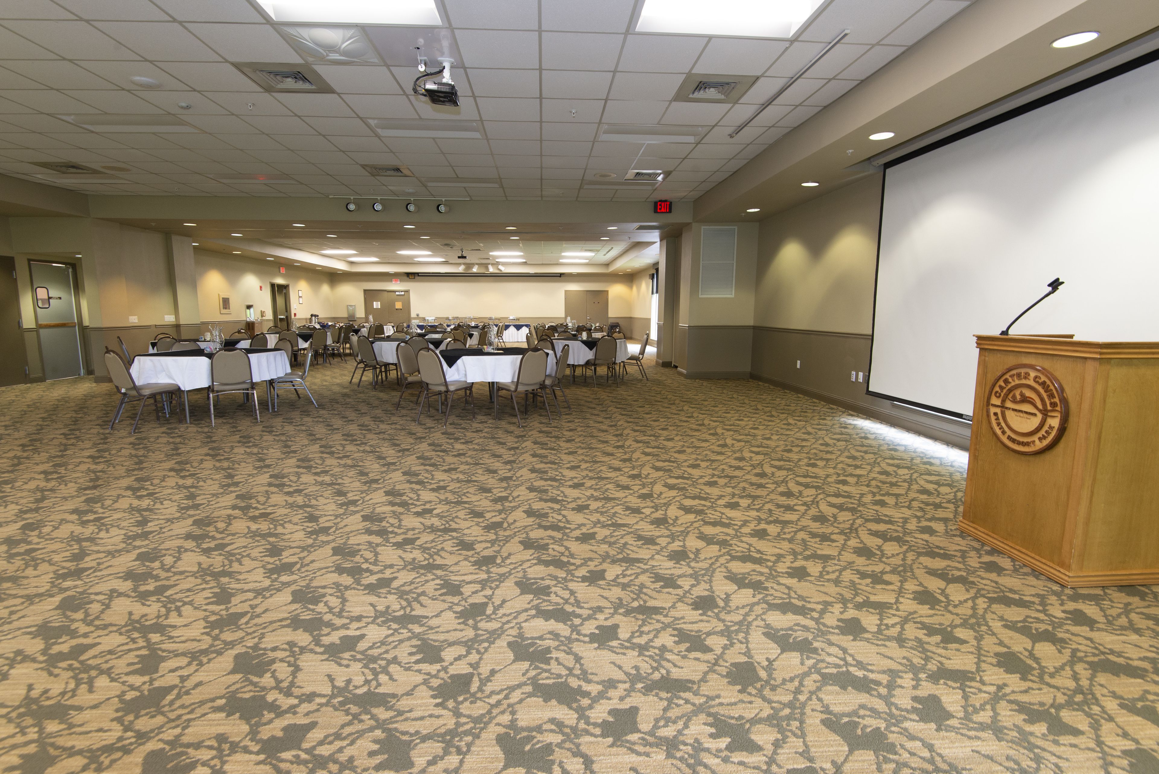 A conference room with tables and chairs, a podium, and a projection screen.