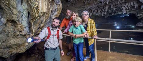 A group of people inside a cave with rocky walls and a railing overlooking a body of water.