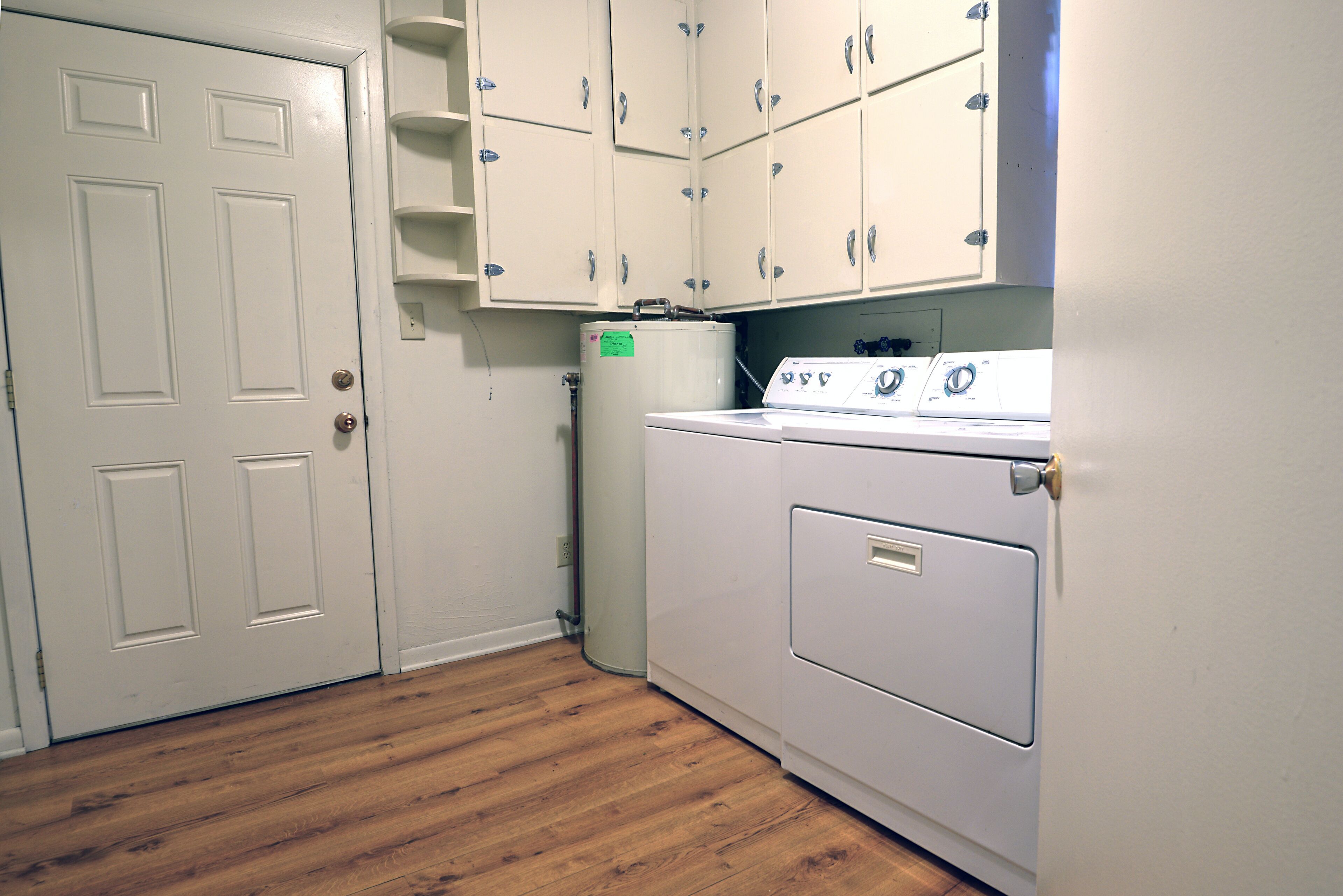 A laundry room with a washer and dryer, wooden flooring, and white cabinets.