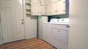 A laundry room with a washer and dryer, wooden flooring, and white cabinets.